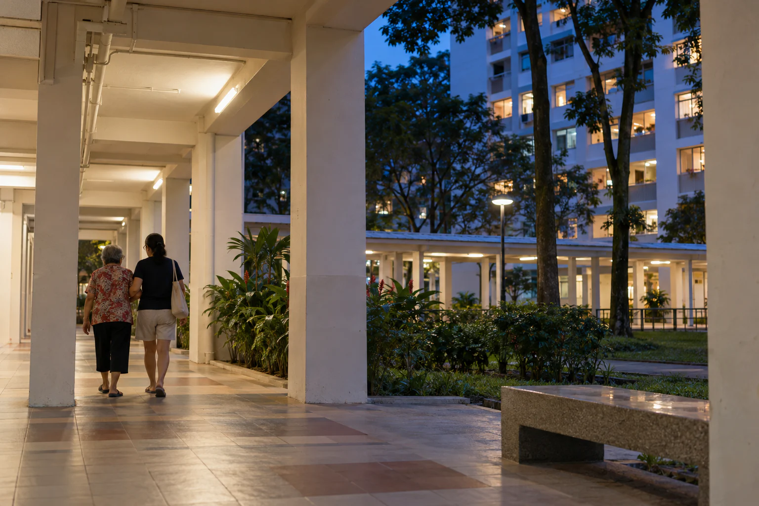 An older adult and a caregiver walk through an HDB void deck at dusk.